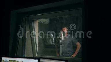 男歌手戴着耳机唱着歌进入录音室的麦克风。 展示商业理念。 一名成年男子录制